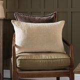Haze Plain Velvet Cushion in Quartz, a rectangular quilted velvet cushion with ribbed texture, shown on an armchair with a brown velvet cushion behind it in a living room setting.