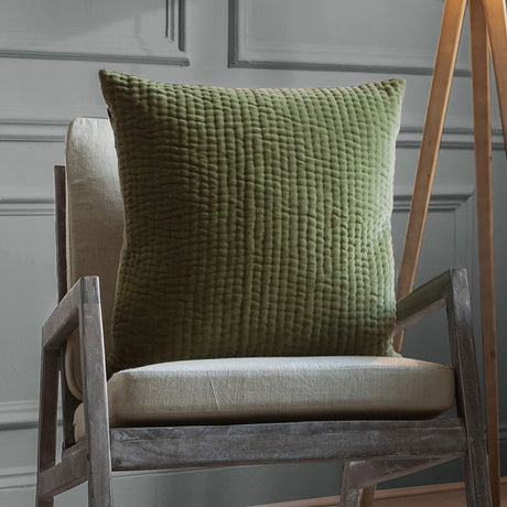 Haze Plain Velvet Cushion in sage green with quilted vertical channel texture, shown on a wooden armchair with linen upholstery.