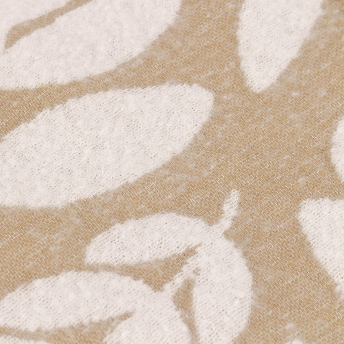 Close-up of the Hazel Botanical Polyester Throw in oatmeal, showing a woven leaf pattern in soft white against a beige textured ground.