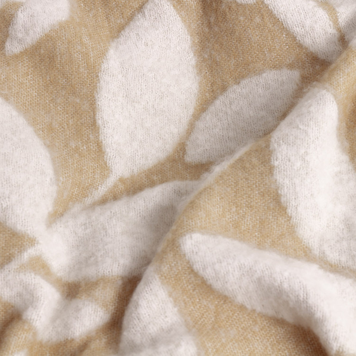 Close-up of the Hazel Botanical Polyester Throw in oatmeal, showing a soft white leaf pattern on a beige woven ground with a folded, textured drape.
