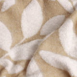 Close-up of the Hazel Botanical Polyester Throw in oatmeal, showing a soft white leaf pattern on a beige woven ground with a folded, textured drape.