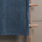 Haze Velvet Cotton Throw in bluebell blue, quilted cotton velvet with textured stitched rows, draped over a wooden ladder against a grey wall.