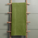Haze Velvet Cotton Throw in grass green, hand-quilted cotton velvet with rippled texture and smooth velvet border, draped over a wooden ladder rack.