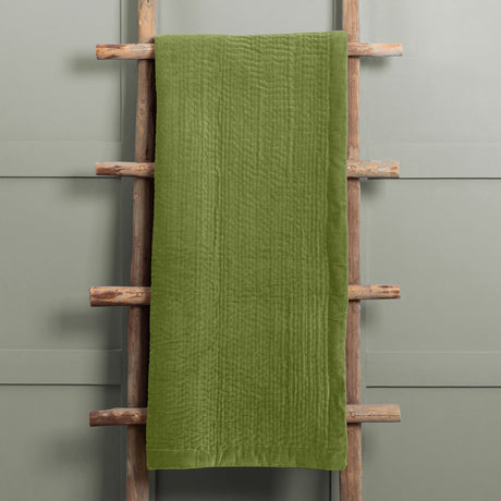 Haze Velvet Cotton Throw in grass green, hand-quilted cotton velvet with rippled texture and smooth velvet border, draped over a wooden ladder rack.