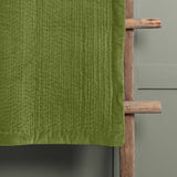 Haze Velvet Cotton Throw in grass green, hand-quilted cotton velvet with rippling texture and smooth border edge, draped over a wooden ladder against a grey wall.