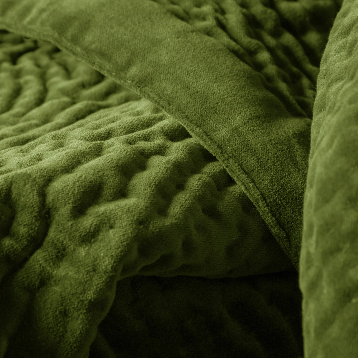 Close-up of the Haze Velvet Cotton Throw in grass green, showing hand-quilted rippling texture and a smoother velvet border edge.