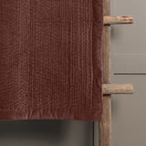 Haze Velvet Cotton Throw in persimmon brown, hand-quilted for a rippled texture, draped over a wooden ladder against a grey wall.