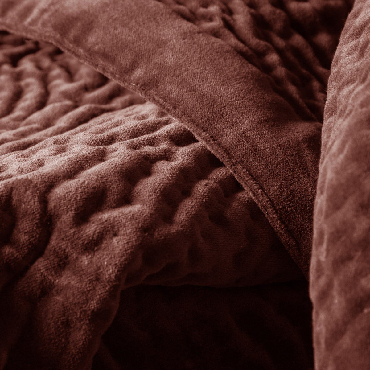 Close-up of the Haze Velvet Cotton Throw in Persimmon, showing its hand-quilted texture and stitched seam in a rich brown-red cotton velvet.