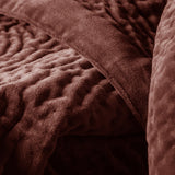 Close-up of the Haze Velvet Cotton Throw in Persimmon, showing its hand-quilted texture and stitched seam in a rich brown-red cotton velvet.