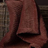 Haze Velvet Cotton Throw in Persimmon, hand-quilted brown-red cotton velvet with rippled texture, draped over a woven wicker basket.