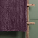 Haze Velvet Cotton Throw in plum, hand-quilted with ribbed texture, draped over a wooden ladder against a green panelled wall.