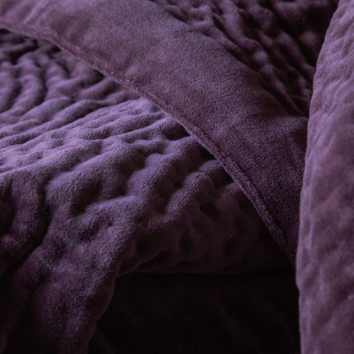 Close-up of the Haze Velvet Cotton Throw in plum, showing hand-quilted cotton velvet with rippled channel texture and a plain folded edge.