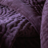 Close-up of the Haze Velvet Cotton Throw in plum, showing hand-quilted cotton velvet with rippled channel texture and a plain folded edge.