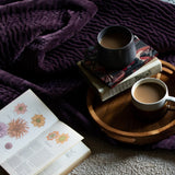 Haze Velvet Cotton Throw in plum, quilted texture draped over a bed, styled with a botanical book and cups of tea on a wooden tray.