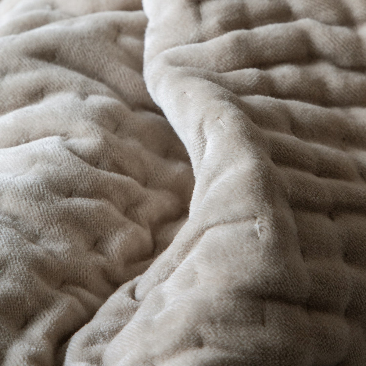 Close-up of the Haze Velvet Cotton Throw in Quartz, showing hand-quilted, wave-like stitching across pale stone-beige velvet cotton fabric.