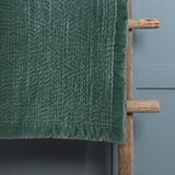 Haze Velvet Cotton Throw in seafoam green, hand-quilted cotton with a velvet pile and finished edge, draped over a wooden rail against a pale blue wall.