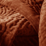 Close-up of the Haze Velvet Cotton Throw in rust-orange, showing a hand-quilted cotton velvet surface with soft undulating channels and a smooth folded edge.