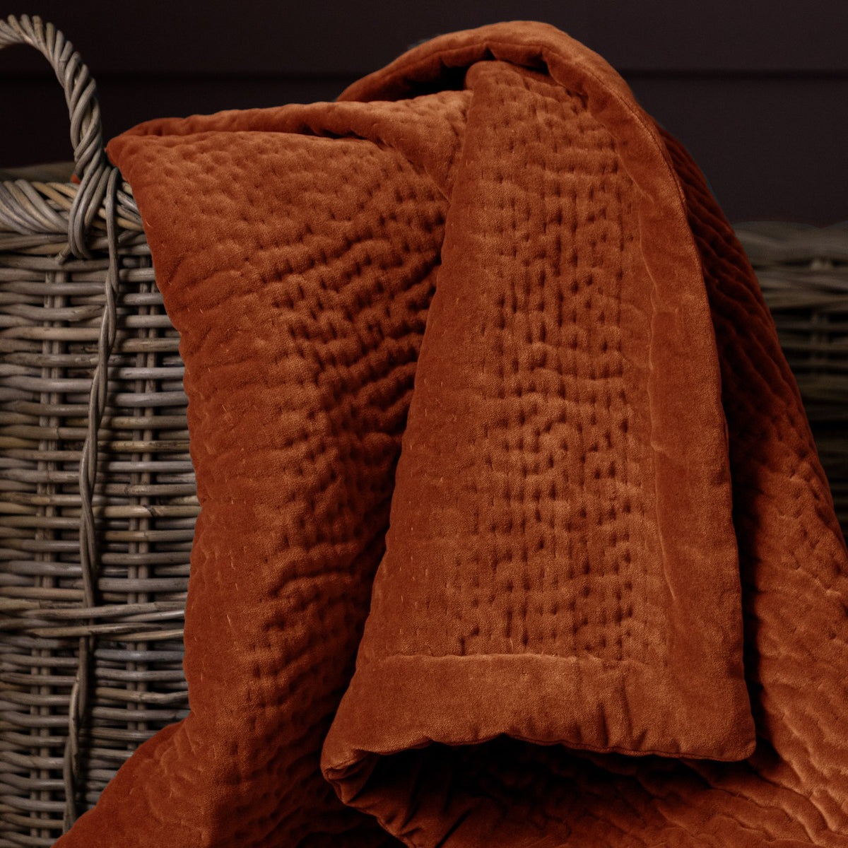 Haze Velvet Cotton Throw in rust-orange, hand-quilted cotton velvet with rippled channel texture, draped over a woven basket.
