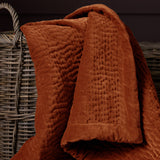 Haze Velvet Cotton Throw in rust-orange, hand-quilted cotton velvet with rippled channel texture, draped over a woven basket.