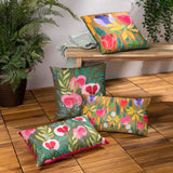 House of Bloom Floral Polyester Cushion in olive with pink poppy print and bright pink reverse, shown among coordinating patterned cushions on a wooden deck.