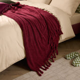 Harlan Borg Sherpa Plain Polyester Throw in burgundy, draped over a bed with tasselled fringe edge, styled with cream bedding in a bedroom setting.