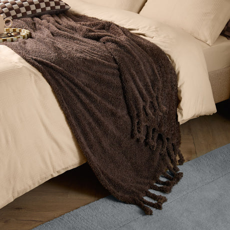 Harlan Borg Sherpa Plain Polyester Throw in chocolate brown, textured curly-pile fabric with twisted tassel edge, draped over a bed with cream bedding.