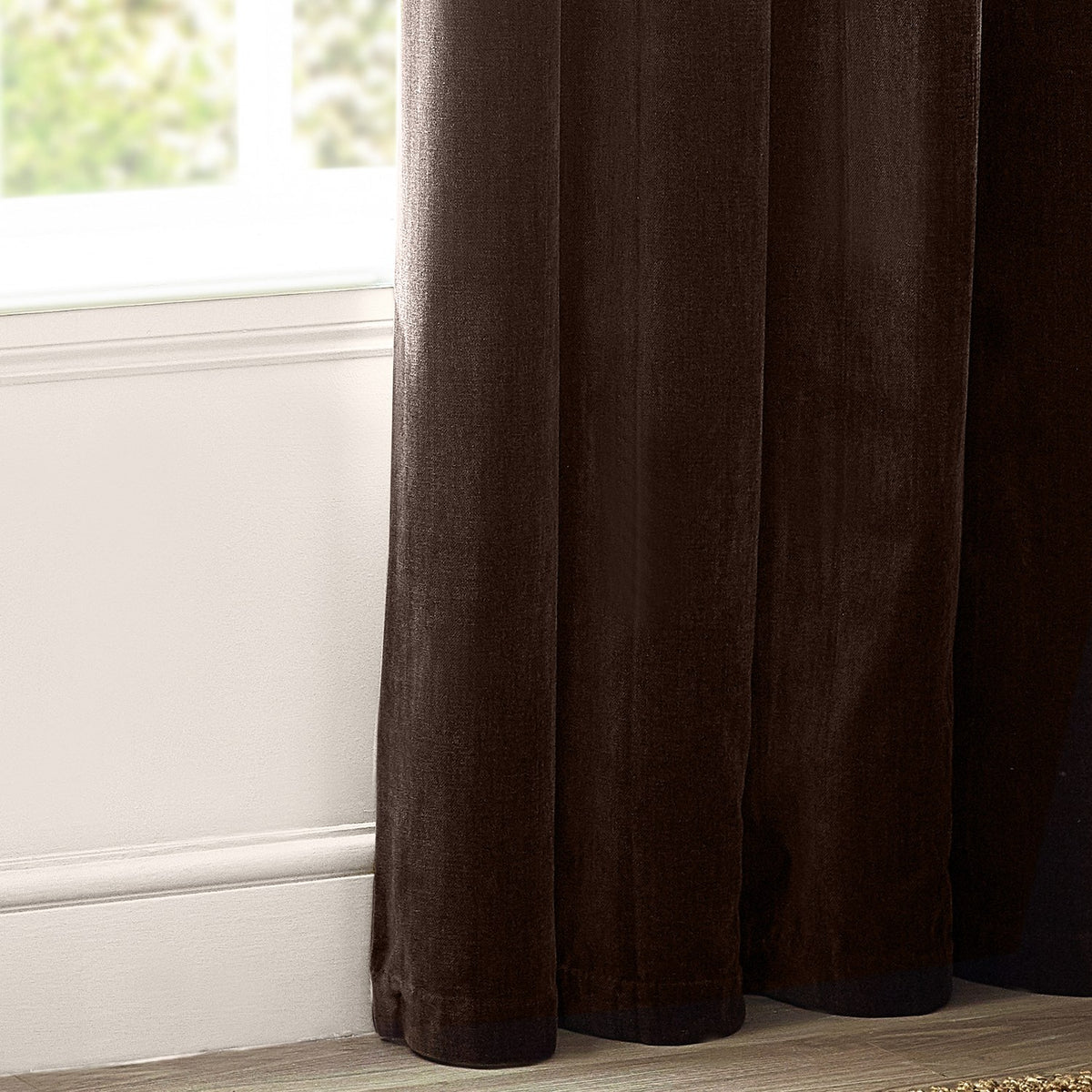 Heavy chenille velvet eyelet curtains in deep brown, showing dense pile fabric and lined panel folds pooling near a window with white skirting board.