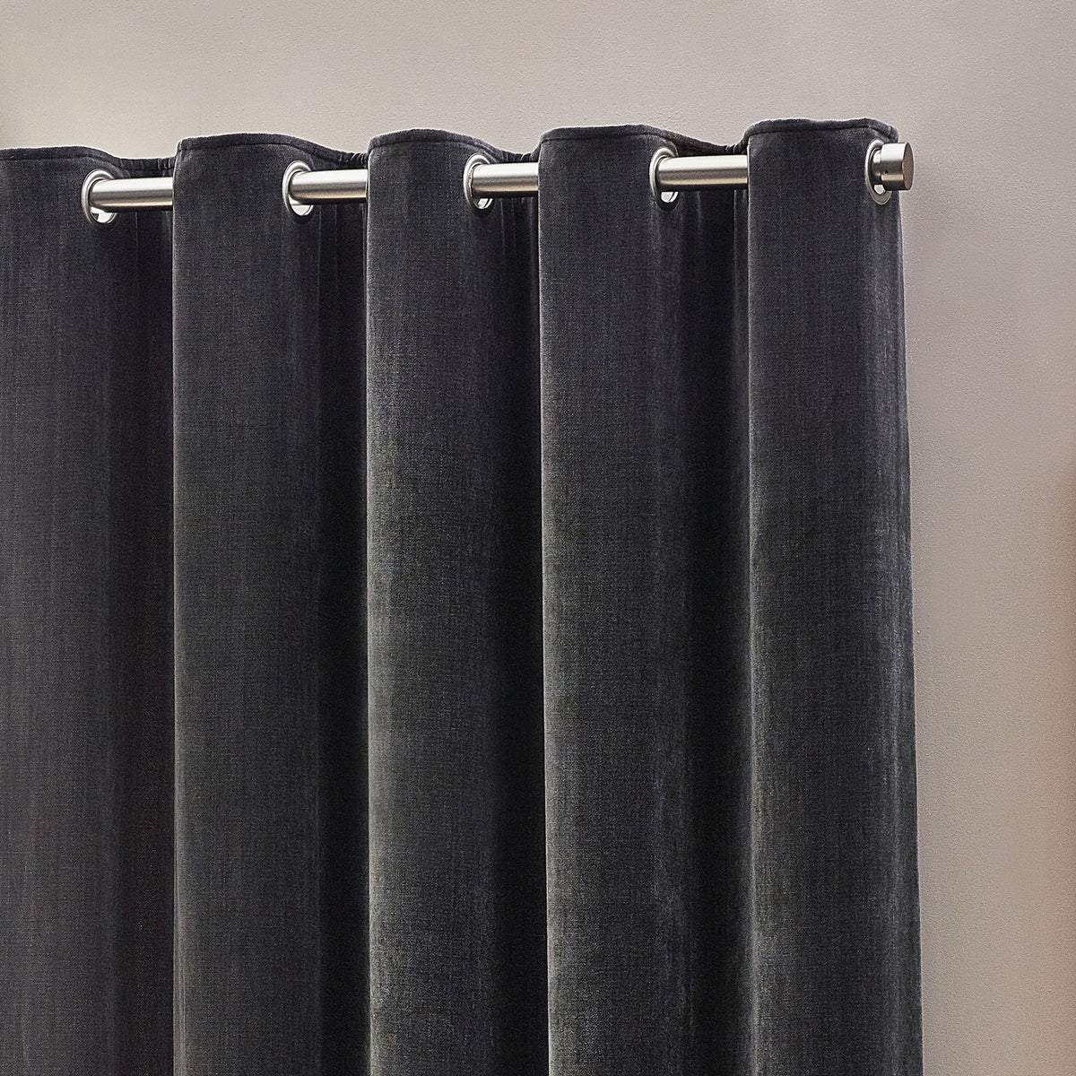 Charcoal chenille velvet eyelet curtains hanging in deep folds on a brushed metal pole, showing the soft piled fabric texture against a light neutral wall.