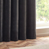 Charcoal heavy chenille velvet eyelet curtains hanging in deep, even folds beside a bright window, shown above a herringbone wood floor.