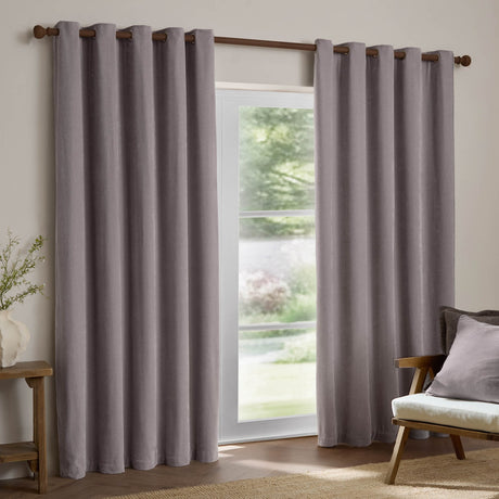 Heavy chenille velvet eyelet curtains in mauve, hung on a wooden rod either side of a glass door in a living room, showing soft pile texture and grommet header.