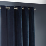 Close-up of navy chenille velvet eyelet curtains with brushed metal grommet rings hung on a matching pole against a dark grey wall.