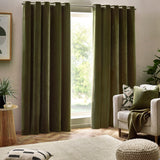 Olive chenille velvet eyelet curtains hanging in deep folds either side of a window, shown in a living room with a beige armchair and cushions.