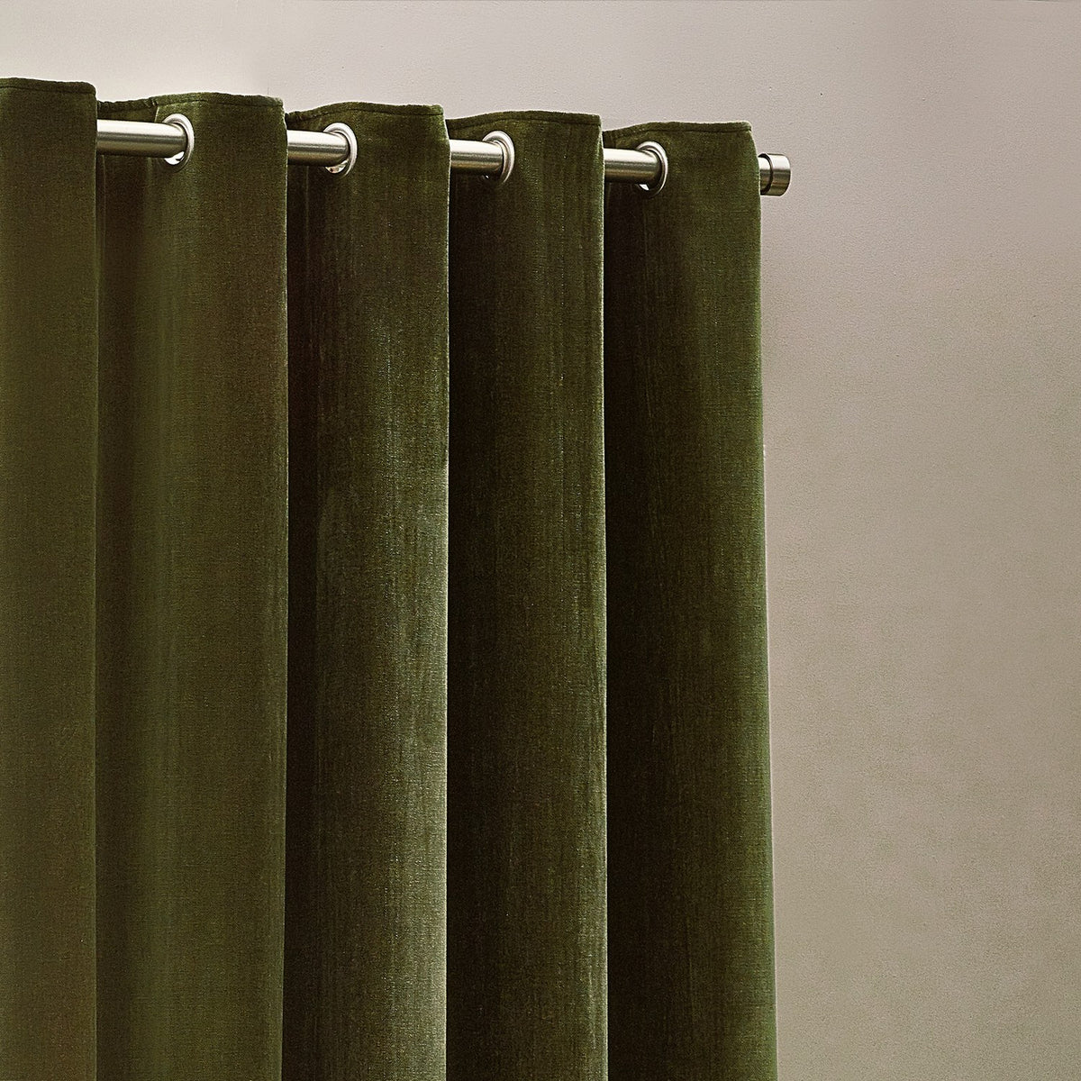 Close-up of Heavy Chenille Velvet Lined Eyelet Curtains in olive, showing brushed metal eyelets on a rod against a plain neutral wall.