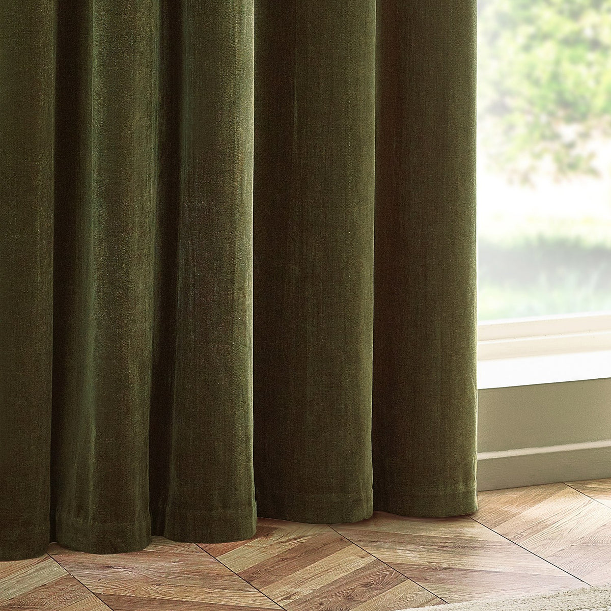Heavy Chenille Velvet Lined Eyelet Curtains in olive green, shown hanging in deep folds beside a window with wooden herringbone flooring.