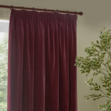 Heavy chenille velvet pencil pleat curtains in beetroot red, hung from a pole with gathered pleat heading tape, shown against a window in a living room setting.