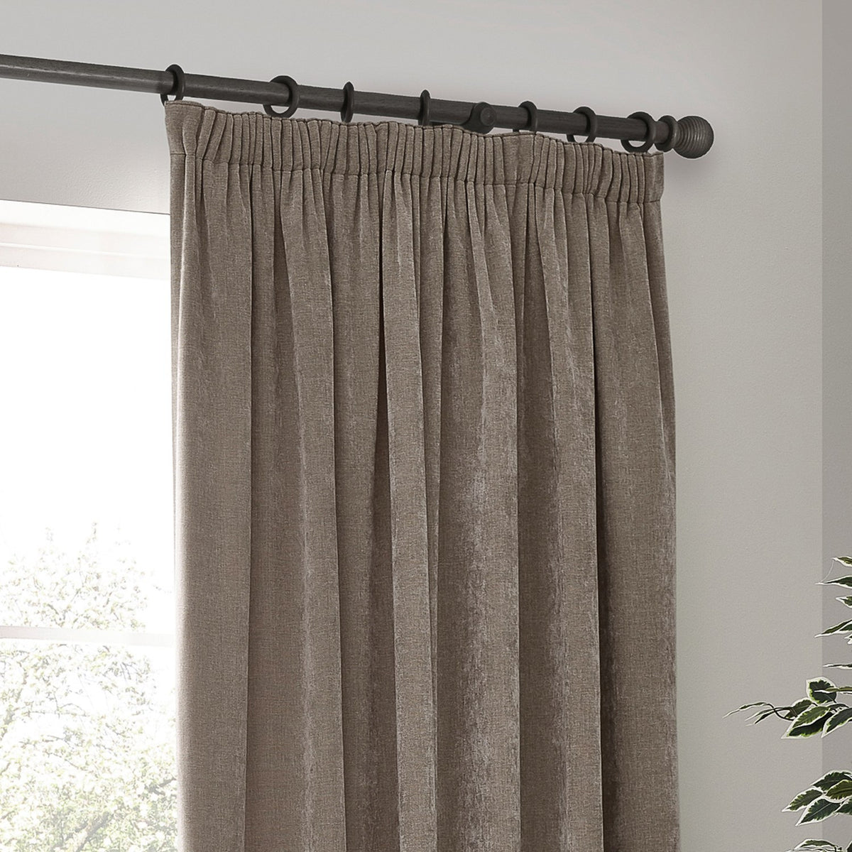 Heavy Chenille Plain Velvet Pencil Pleat Curtains in greige, hung on a dark metal pole with pencil pleat heading, shown draping in soft folds by a window.