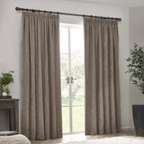 Pair of pencil pleat curtains in greige chenille velvet, hanging from a dark metal pole beside a glass door in a living room setting.