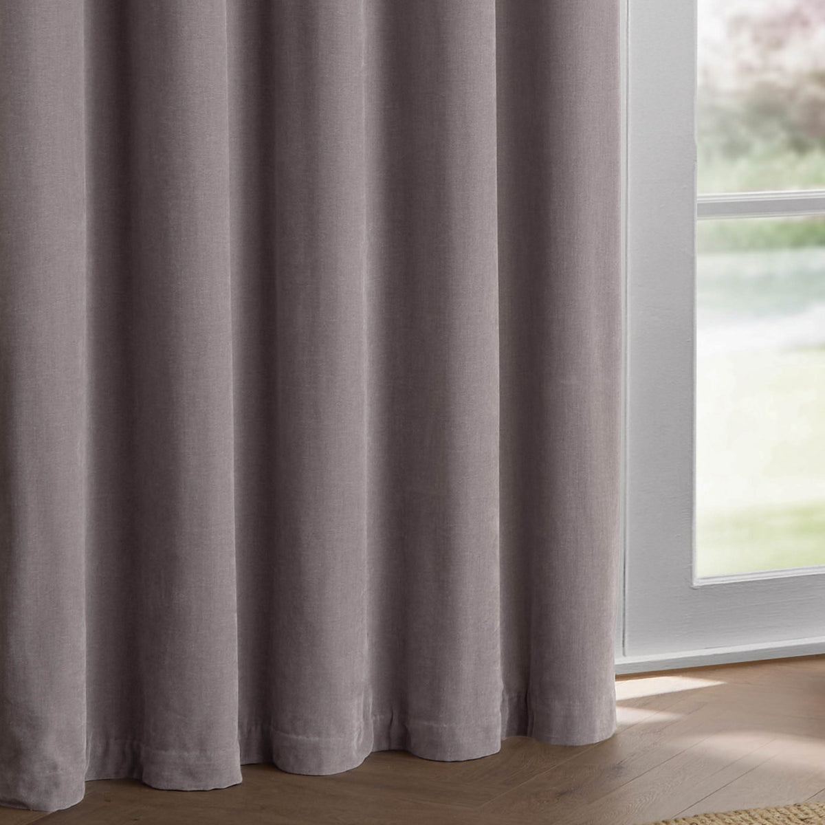 Mauve chenille pencil pleat curtains with soft velvety folds, shown hanging beside a window in a room with wooden flooring.