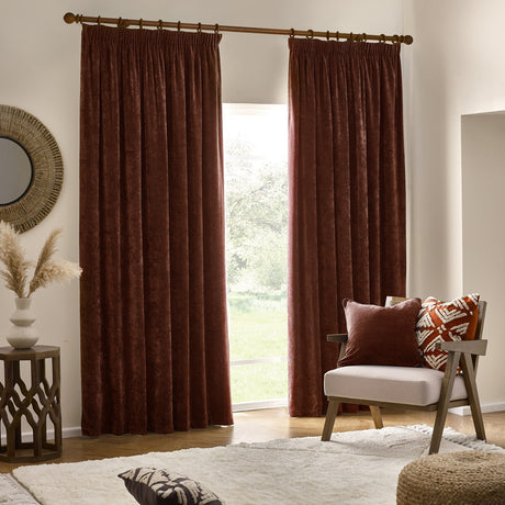 Nutmeg-red pencil pleat curtains in heavy chenille velvet fabric, hung from a wooden pole in a living room beside a patio door.