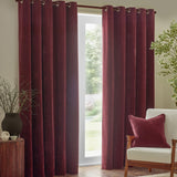 Square beetroot red velvet cushion with piped edge on a cream armchair, styled with burgundy curtains in a living room setting.