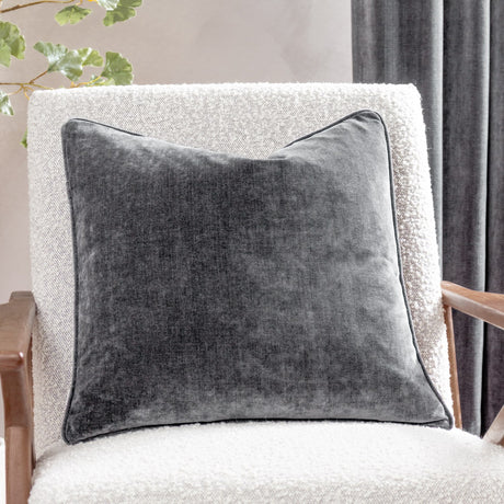 Charcoal heavy chenille velvet cushion with piped edge trim, shown on a light boucle armchair in a living room setting.
