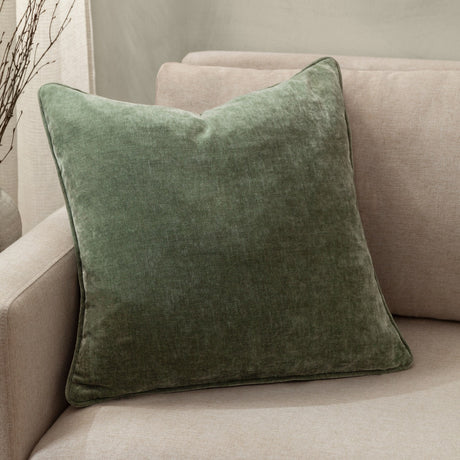 Square heavy chenille velvet cushion in eucalyptus green with piped edges, shown on a beige upholstered sofa in a living room setting.