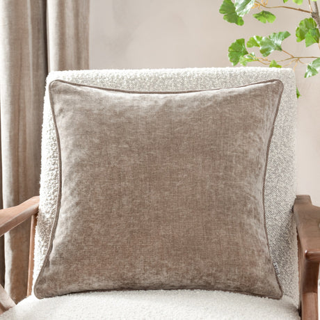Square greige chenille velvet cushion with piped edge trim, shown on a cream boucle armchair in a living room setting.