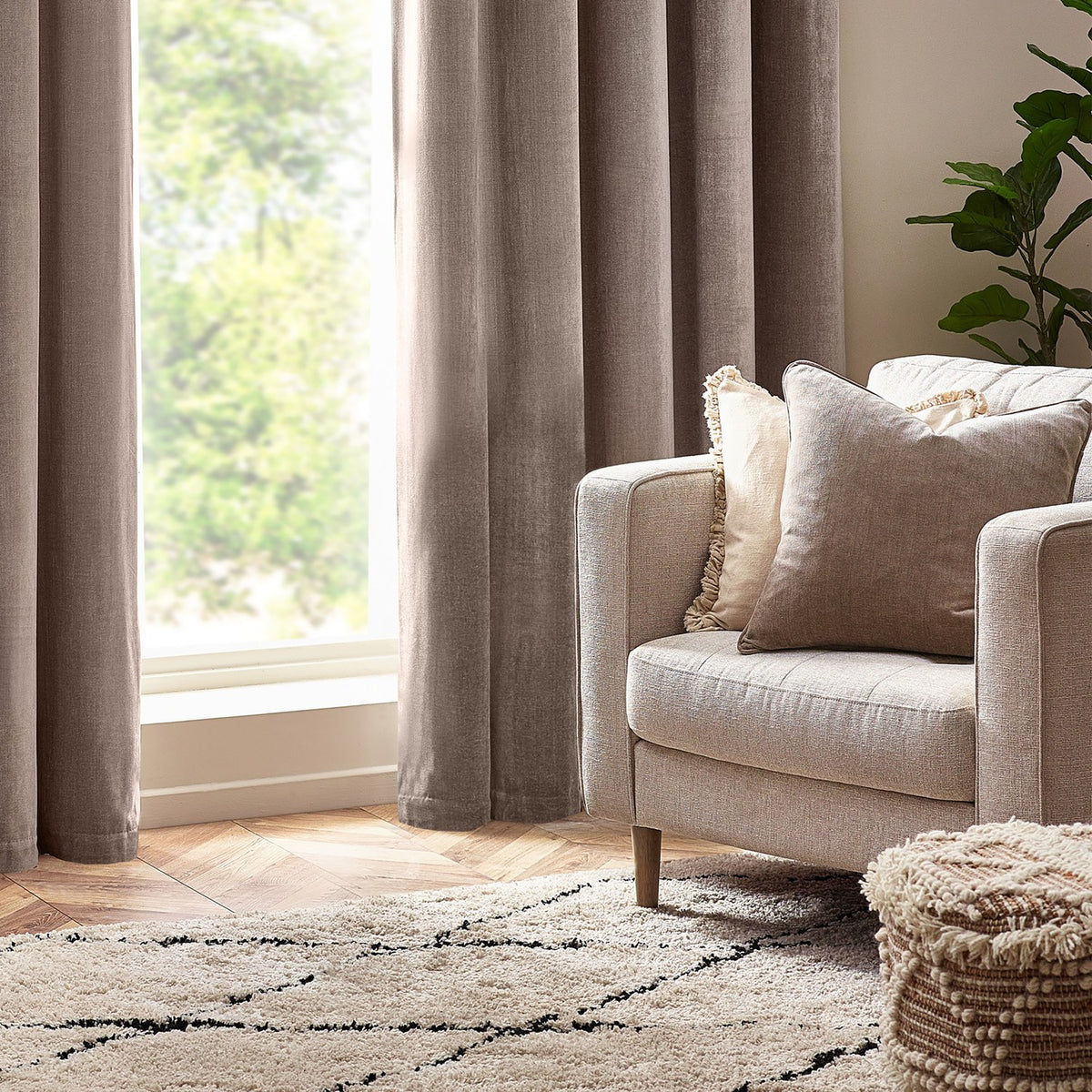 Heavy Chenille Eyelet Velvet Cushion in greige on a beige armchair, styled with a fringed cream cushion in a living room with curtains and a patterned rug.