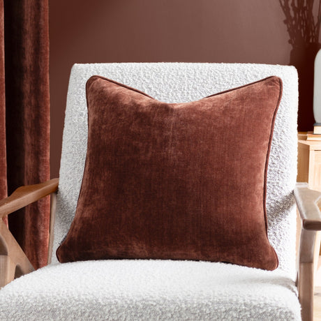 Square Heavy Chenille Eyelet Velvet Cushion in Nutmeg brown, shown on a white boucle armchair against a reddish-brown wall.
