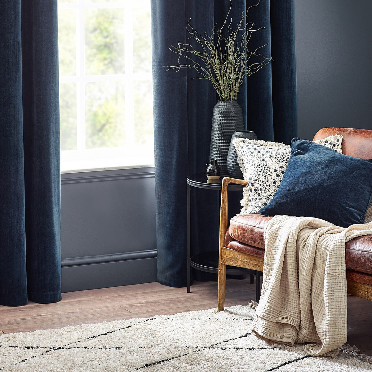 Navy Heavy Chenille Velvet Cushion with piped trim on a leather sofa, styled with cream throws and patterned pillows in a living room setting.