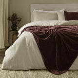 Heavy Chenille Eyelet Velvet Throw in Beetroot draped over a bed with cream bedding, layered atop white and beige pillows in a neutral-toned bedroom.