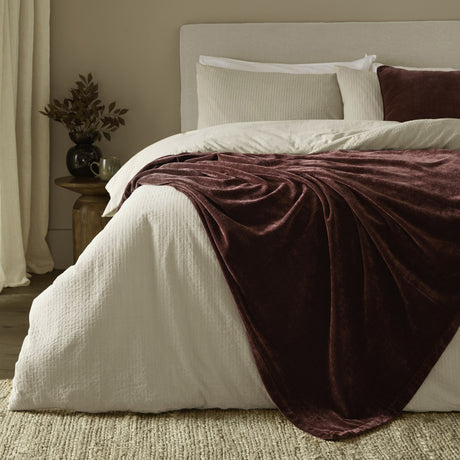 Heavy Chenille Eyelet Velvet Throw in Beetroot draped over a bed with cream bedding, layered atop white and beige pillows in a neutral-toned bedroom.