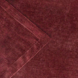 Close-up of a heavy chenille velvet throw in deep beetroot red, showing a folded corner with hemmed edge and the mottled, wine-toned pile texture.