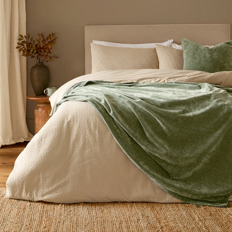 Heavy Chenille Eyelet Velvet Throw in eucalyptus green draped over a beige bed with matching cushions, styled in a bedroom with a jute rug and wooden side table.